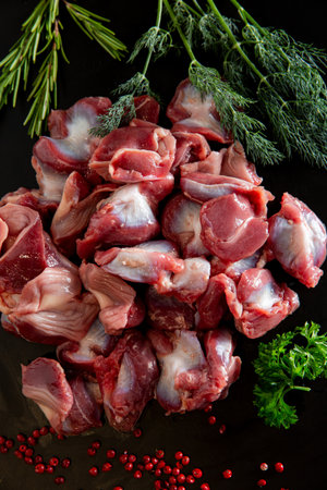 Flat lay of cleaned raw chicken gizzards on a black surface, decorated with peppercorns and greens. Rich in flavor, popular in traditional dishes.の写真素材