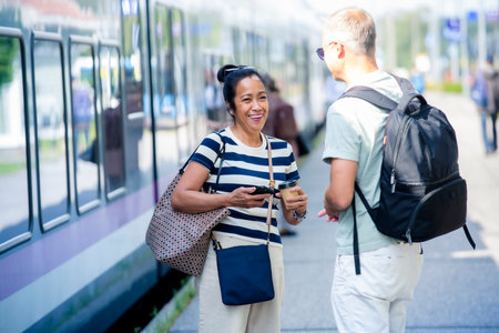 Happy middle aged Asian woman laughing with man on train platform, symbolizing diversity, connection, modern city lifestyle, and urban commuting.の写真素材