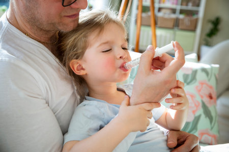 Father giving sick toddler fever medicine with oral syringe at home. Flu season, childcare, illness treatment, healthcare and family support.の写真素材