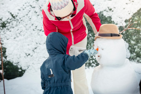 Grandmother and toddler building a snowman in snowy backyard. Joyful winter day, family bonding, healthy outdoor activity, seasonal lifestyleの写真素材