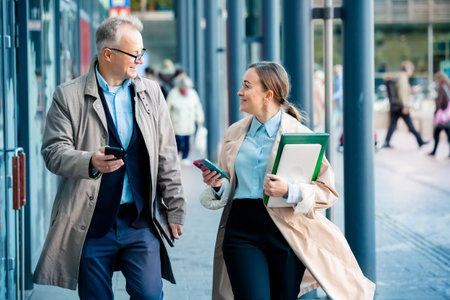 Business man and woman walking in city street, smiling and talking with laptop and coffee. Urban teamwork and success concept.の写真素材
