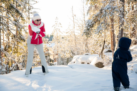 Healthy grandmother and toddler play in snowy forest, tossing snow, enjoying golden winter light, family bonding, and active outdoor fun.の写真素材