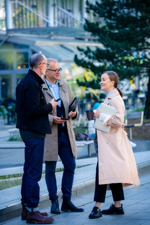 Urban business lifestyle moment: mid-age professionals meeting outdoor, collaborating with laptop and phones, smiling and discussing work over coffeeの写真素材