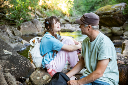 Family hikers resting by a forest stream during mountain trekking. Father and teenage daughter enjoying outdoor adventure, eco tourism, and active lifestyle in natural landscape in Norway.の写真素材