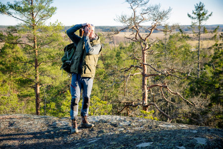 Male hiker taking photos with vintage camera on scenic cliff in Finland. Travel photography,...