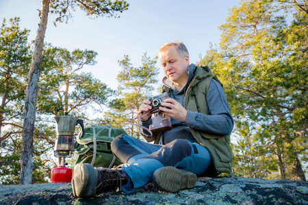 Male hiker taking photos with vintage camera on scenic cliff in Finland. Travel photography, adventure tourism, outdoor lifestyleの写真素材