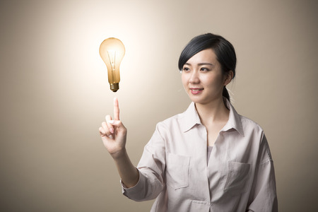 Young woman having light bulb floating above firefingerの写真素材