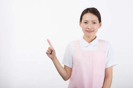 A young woman in a white coat and apron smiling with her index finger up in front of a white background.の写真素材