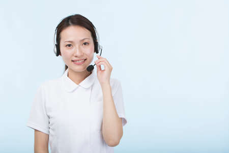 A young woman in a white coat smiling with a headset in front of a light blue backgroundの写真素材