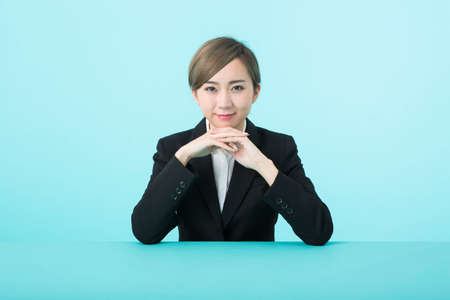A young woman in a suit with her elbows on a green table and a smile on her chin.の写真素材
