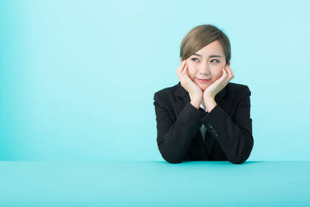 A young woman in a suit with her elbows on a green table and a smile on her chin.の写真素材