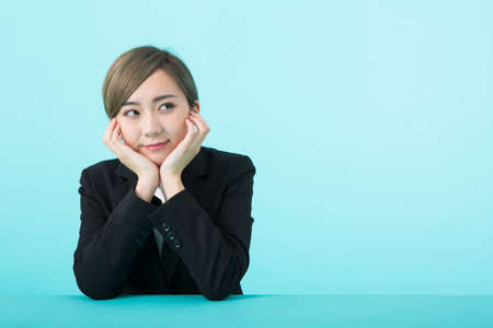 A young woman in a suit with her elbows on a green table and a smile on her chin.の写真素材