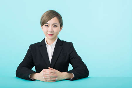 a young woman in a black suit smiling with her hands on a green tableの写真素材