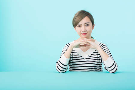 A young woman in white and black striped clothes with elbows on her green deskの写真素材