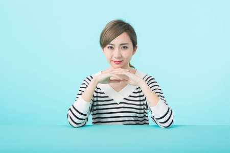 A young woman in white and black striped clothes with elbows on her green deskの写真素材