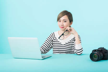 A young woman in white and black striped clothes smiling with glasses in front of her computer at a yellow-green deskの写真素材