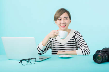 A young woman in white and black striped clothes smiling with a cozy cup in front of her computer at...