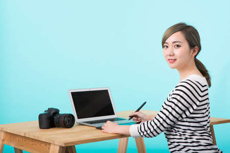 a young woman dressed in white and black striped to operate a computer with a pen tablet on a wooden desk in front of a yellow-green backgroundの写真素材