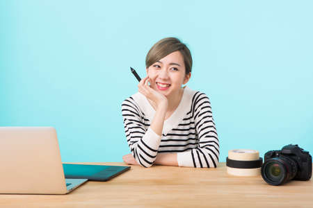 a young woman in white and black striped clothes smiling with her elbows on a wooden desk in front...
