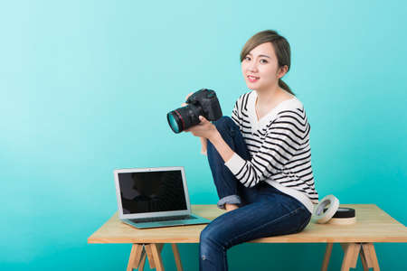 A young woman in white and black striped clothes smiling with a DSLR camera in her hand in front of a yellow-green backgroundの写真素材