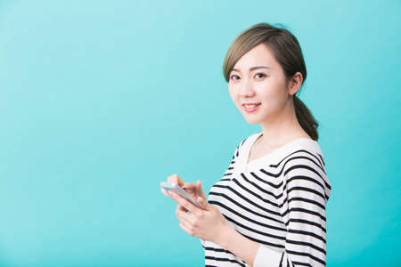A young woman in white and black striped pattern smiling while holding a smartphone in front of a green backgroundの写真素材
