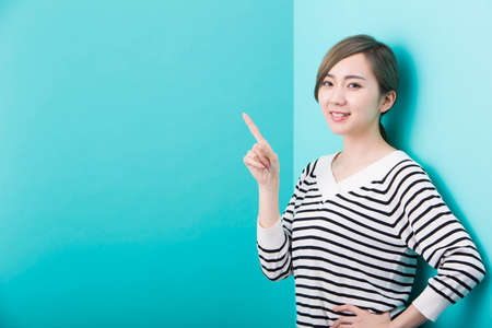 A young woman in white and black striped pattern who smiles with her index finger up in front of a green background.の写真素材