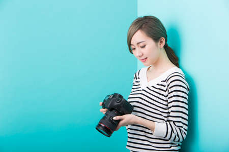 A young woman in white and black striped clothes smiling with a DSLR camera in her hand in front of...