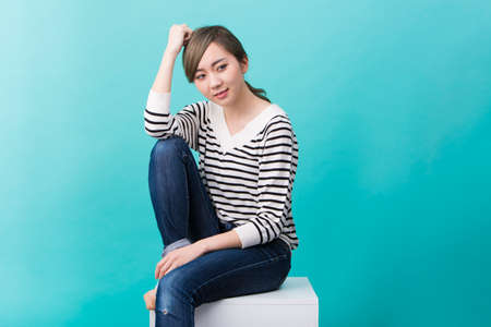 A young woman in white and black striped pattern who smiles as she sits on a white table in front of a blue-green background.の写真素材