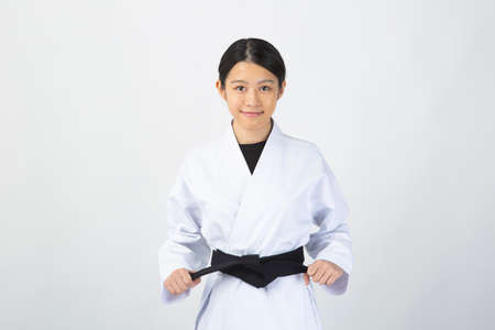 A young woman with dark hair wearing a white dress in front of a white background and smiling while holding a black belt.の写真素材