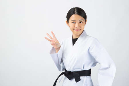 a young woman with dark hair who wears a white dress in front of a white background, tightens her black belt, and smiles with three fingers upの写真素材