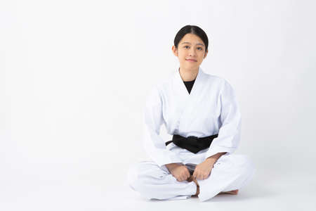 a young woman with dark hair who wears a white dress in front of a white background, tightens her black belt, and smiles with her aguraの写真素材