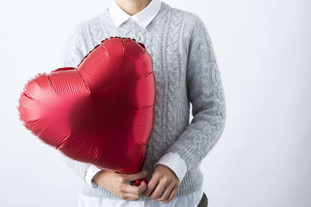 a red heart-shaped balloon in a woman's handの写真素材