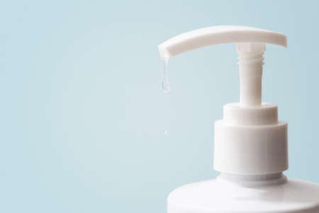 a transparent disinfectant hanging from a white bottle placed in front of a light blue backgroundの写真素材