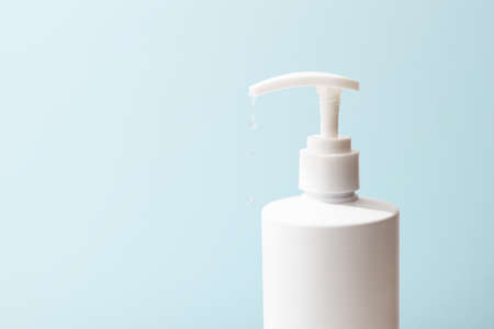 a transparent disinfectant hanging from a white bottle placed in front of a light blue backgroundの写真素材