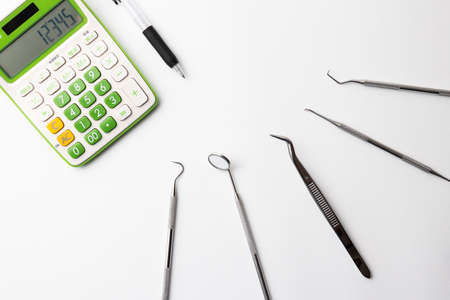 Dental treatment instruments and calculators and pens placed on a white backgroundの写真素材