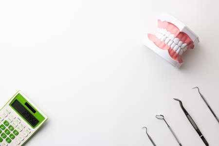 Dental treatment instruments, calculators, and oral models placed on a white backgroundの写真素材