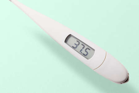 a digital thermometer that displays a slight heat of 37.5 degrees floating on a yellow-green backgroundの写真素材