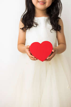 A little girl with black hair has a red heart with both hands.の写真素材