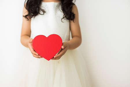 A little girl with black hair has a red heart with both hands.の写真素材