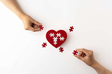 Hands with heart-shaped puzzles and pieces placed on a white backgroundの写真素材