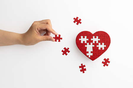 Hands with heart-shaped puzzles and pieces placed on a white backgroundの写真素材