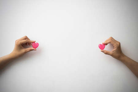 a woman's hand pinching a pink heart-shaped capsule with her finger on a white backgroundの写真素材