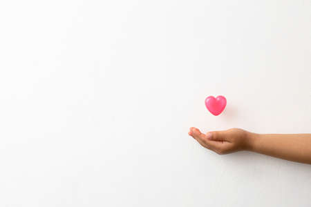 Pink heart-shaped capsule floating on the palm of a child's hand on a white backgroundの写真素材