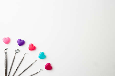 Dental instruments and colorful heart-shaped capsules placed on a white background