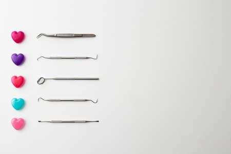 Dental instruments and colorful heart-shaped capsules placed on a white background