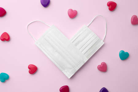 A white mask and a colorful heart-shaped capsule placed in a heart shape on a pink background