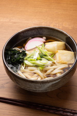 Japanese udon noodle soup with baked rice cakes in bowl on wooden tableの写真素材