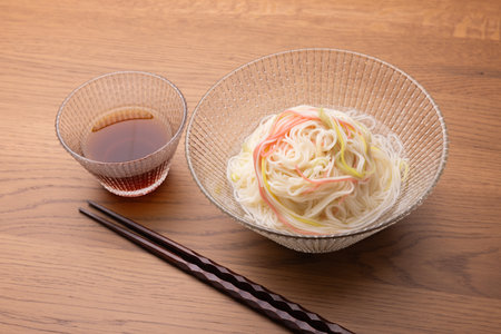 Japanese noodles in a glass bowl on a wooden table with chopsticksの写真素材