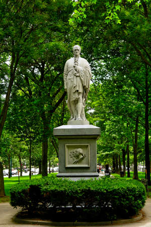statue of learned looking man wrapping his claok around him in the middle of a park surrounded by greenの写真素材