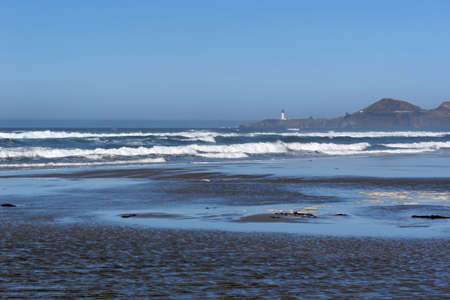 across the beach off in the background a lighthouse sits on the rocks to warn sea captains of the rocky coast of oregonの写真素材